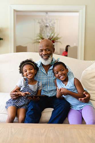 Man sitting on the couch with his two granddaughters, smiling