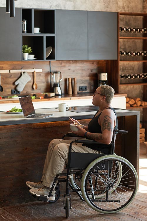 Woman in a wheelchair using a laptop at her kitchen counter