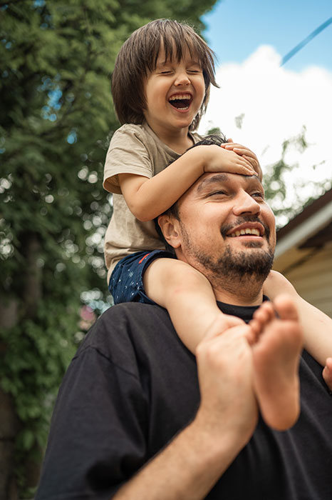 Little boy sitting on top of his dad's shoulders, with a huge smile on his face
