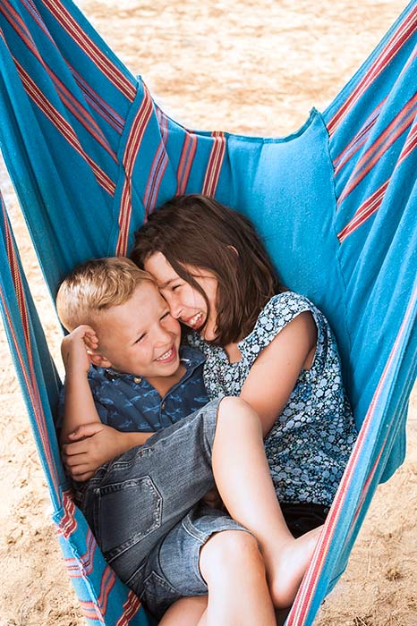 Brother and sister curled up in a hammock together on the beach