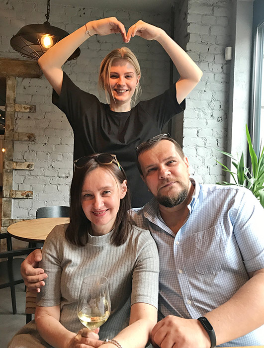 Mother, father, and daughter together at the table with the daughter making a heart shape with her hands behind her parents