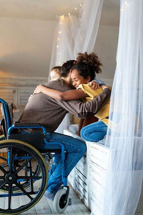 Man in a wheelchair hugging his two daughters