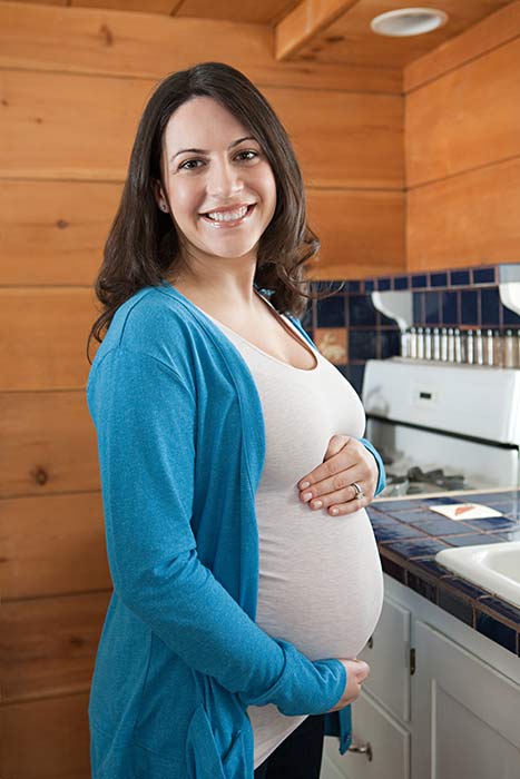 Pregnant woman with her hands on her belly, smiling in her kitchen