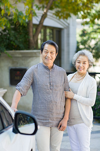 Smiling senior couple standing outside next to their car