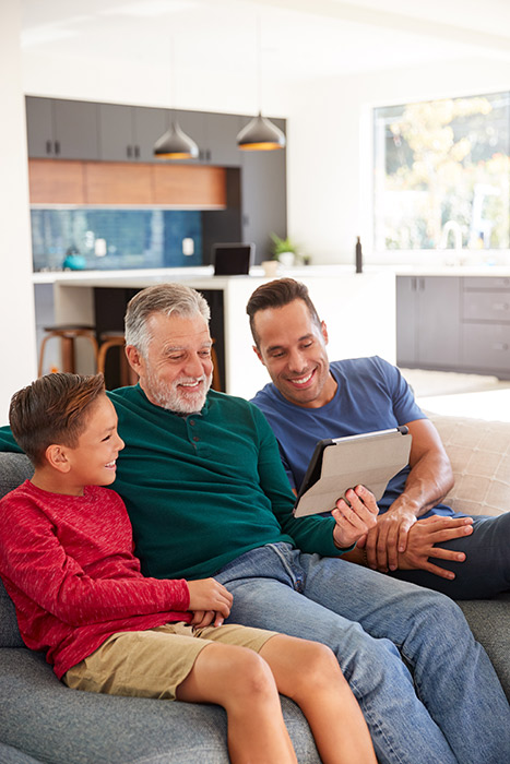 Client Jorge sitting on the couch with his son and grandson, looking at a tablet