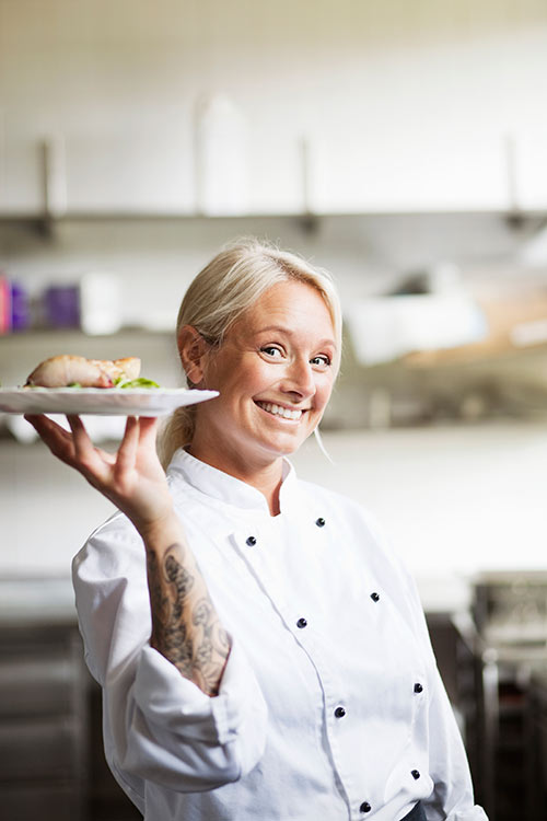 Client Gina dressed in chef's whites holding up a plate of her creations