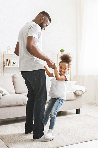 Cute dad and daughter playing together, where the daughter is standing on her dad's feet