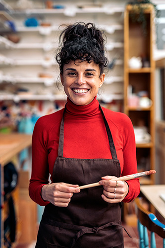 Artist holding her paintbrush and wearing an apron, smiling at the camera