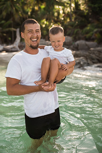 Man in a swimming pool, holding his young son above the water
