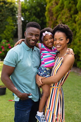 Young mother and father standing outside, holding their young daughter between them