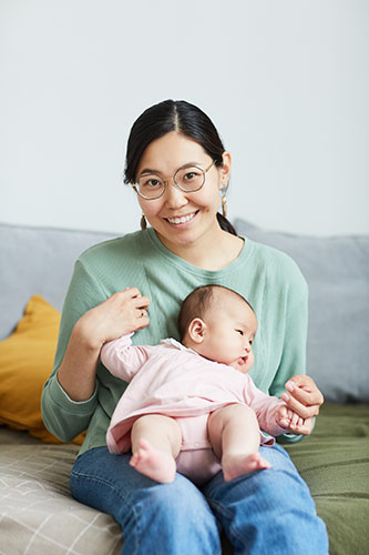 Young mother holding her baby while sitting on her bed, smiling at the camera