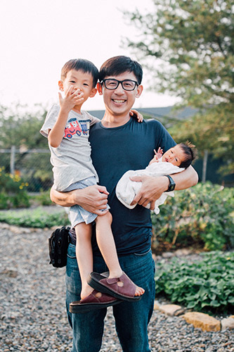 Asian dad holding his young son in one arm and a newborn baby in the other