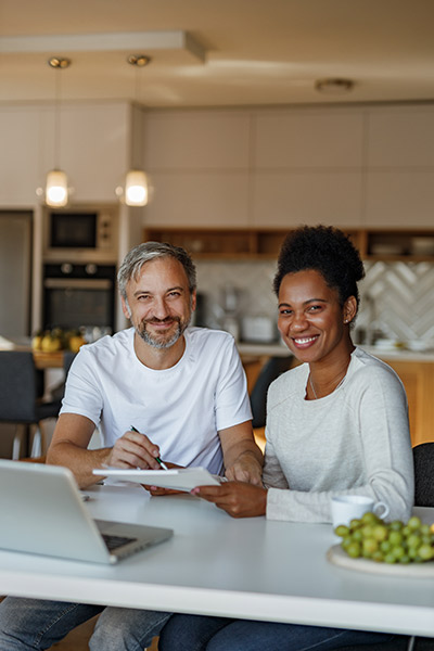 Interracial couple sitting at the kitchen table and researching variable universal life on their laptop