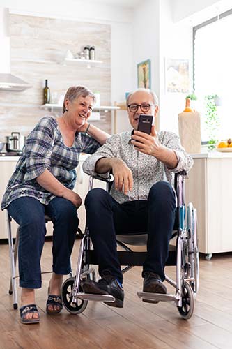 Disabled man in a wheelchair with his wife beside him, looking up information about SSDI and Medicare on his smartphone