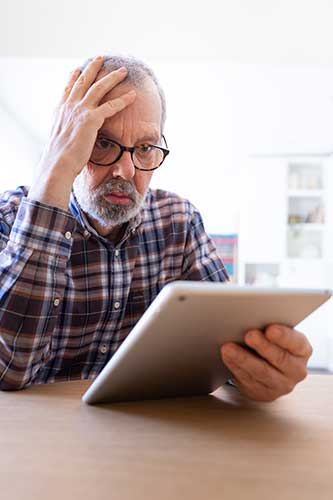Senior man looking at a website about tax liability for government disability insurance with a confused look on his face