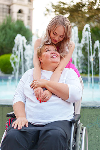Young woman hugging her mom, who is in a wheelchair due to a disability