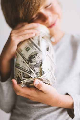 Little boy holding a jar stuffed with hundred dollar bills