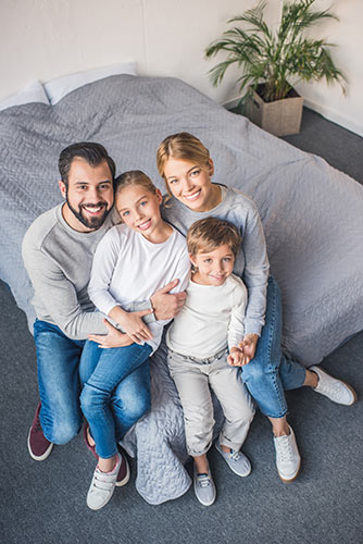 Happy family of four posing for a photo while sitting together on the corner of a bed