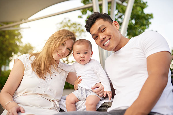 Young smiling couple sitting outside with their baby son