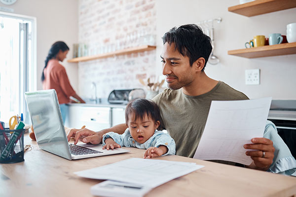 Young father looking up whole life insurance on his laptop while holding his baby on his lap