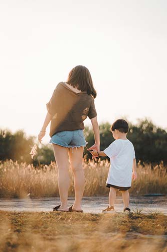 Young mom walking in the park with her son, holding him by the hand