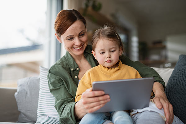 Mom holding her toddler on her lap while researching whole life insurance on her tablet