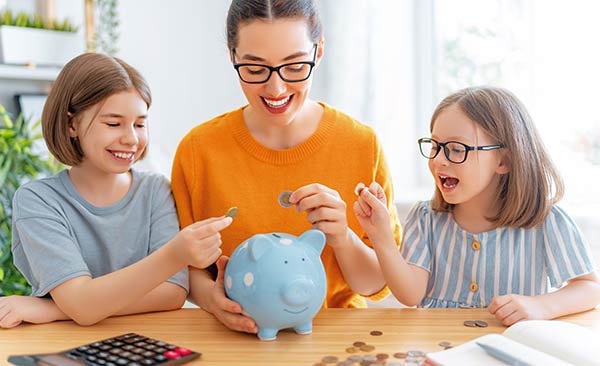 Mom and two daughters putting coins in a piggy bank
