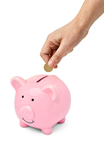 Close-up photo of a hand slipping a coin into a pink piggy bank, symbolizing the savings component of whole life insurance