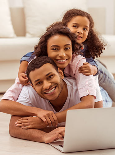 Smiling parents and daughter in their living room, as the dad looks up life insurance quotes online