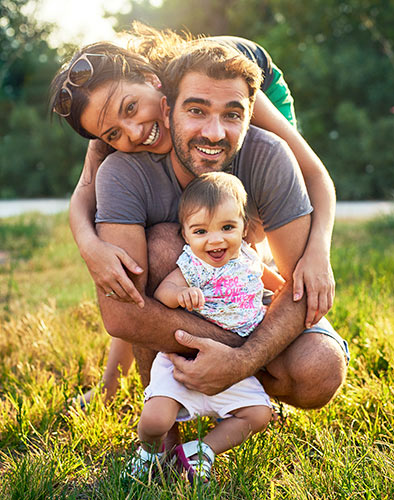Mom, Dad, and their baby daughter smiling while outdoors in a park