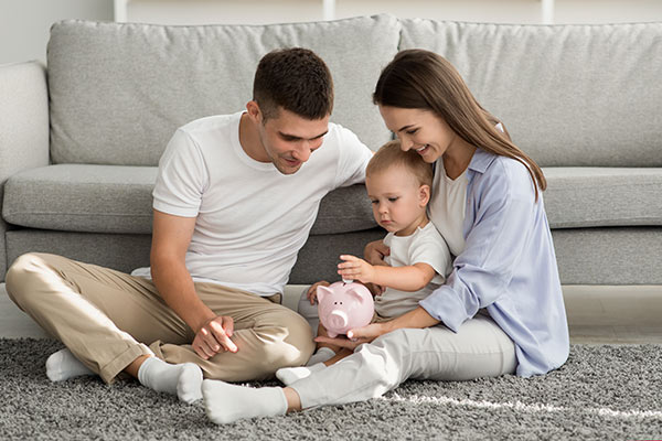 Young parents sitting on the floor with their son, helping him put money in a piggy bank, symbolizing the affordability of term life insurance