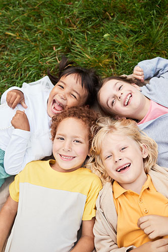 Four kids laying on the grass and laughing, looking up into the camera