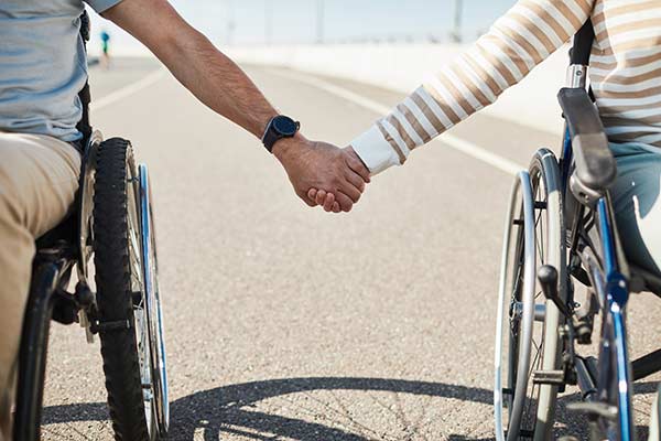 Close-up photo of two people in wheelchairs holding hands