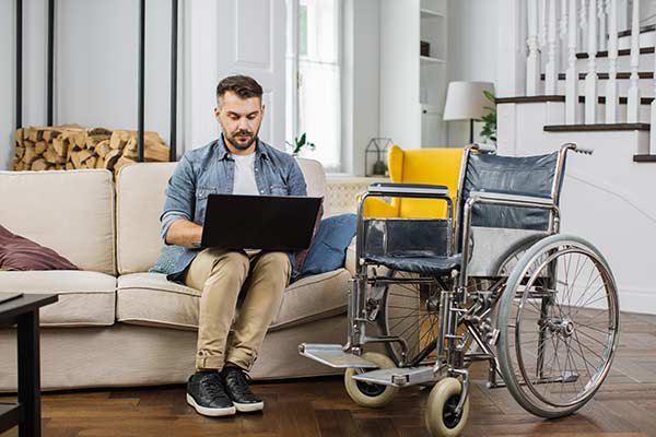 Man sitting on the couch researching a disability insurance definition, with his wheelchair next to the couch