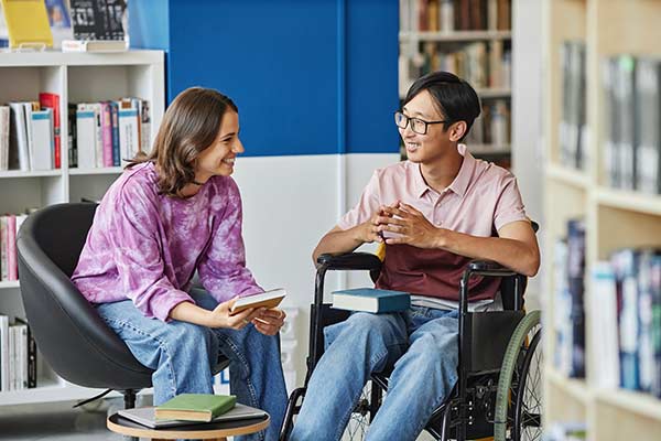 Student in a wheelchair meeting a friend in a library