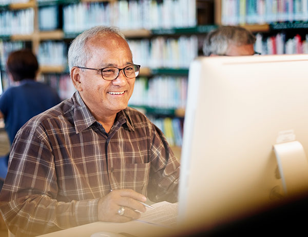 Senior man using a public computer at the library to get life insurance quotes over 50