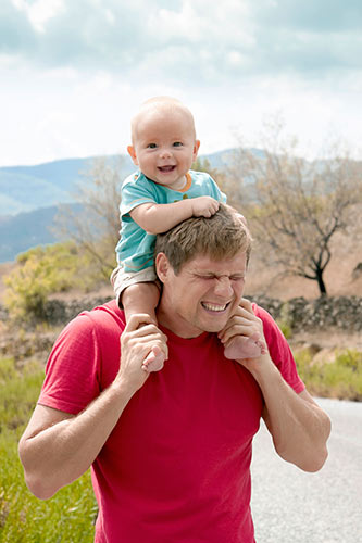 Dad making a funny face while walking in a park with his toddler on his shoulders