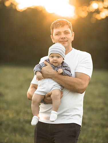 Young dad holding his adorable baby in a park, with the setting sun behind them